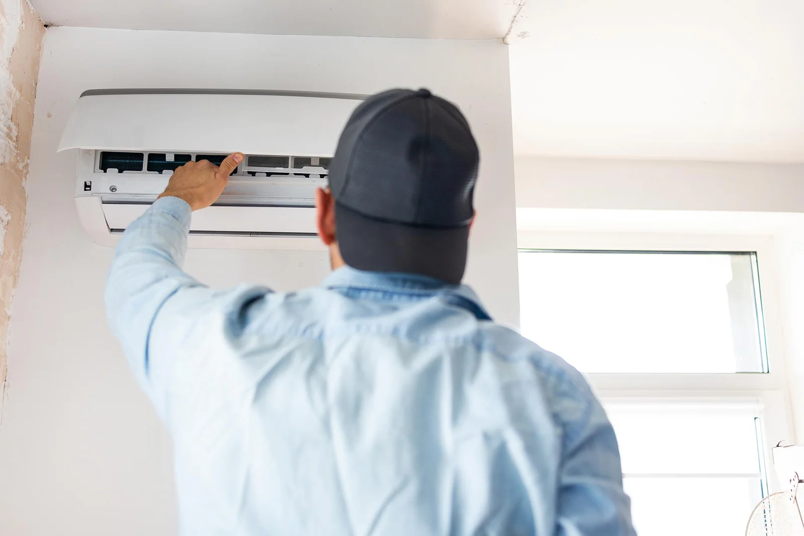 Licensed technician repairs a wall-mounted air conditioning unit inside a Peoria home